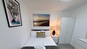 A bedroom with a bed, pillows, a green blanket, a towel, a painting, a lamp, and a wardrobe. - Sleek 1BR Flat  Perfect Getaway (Cardiff)