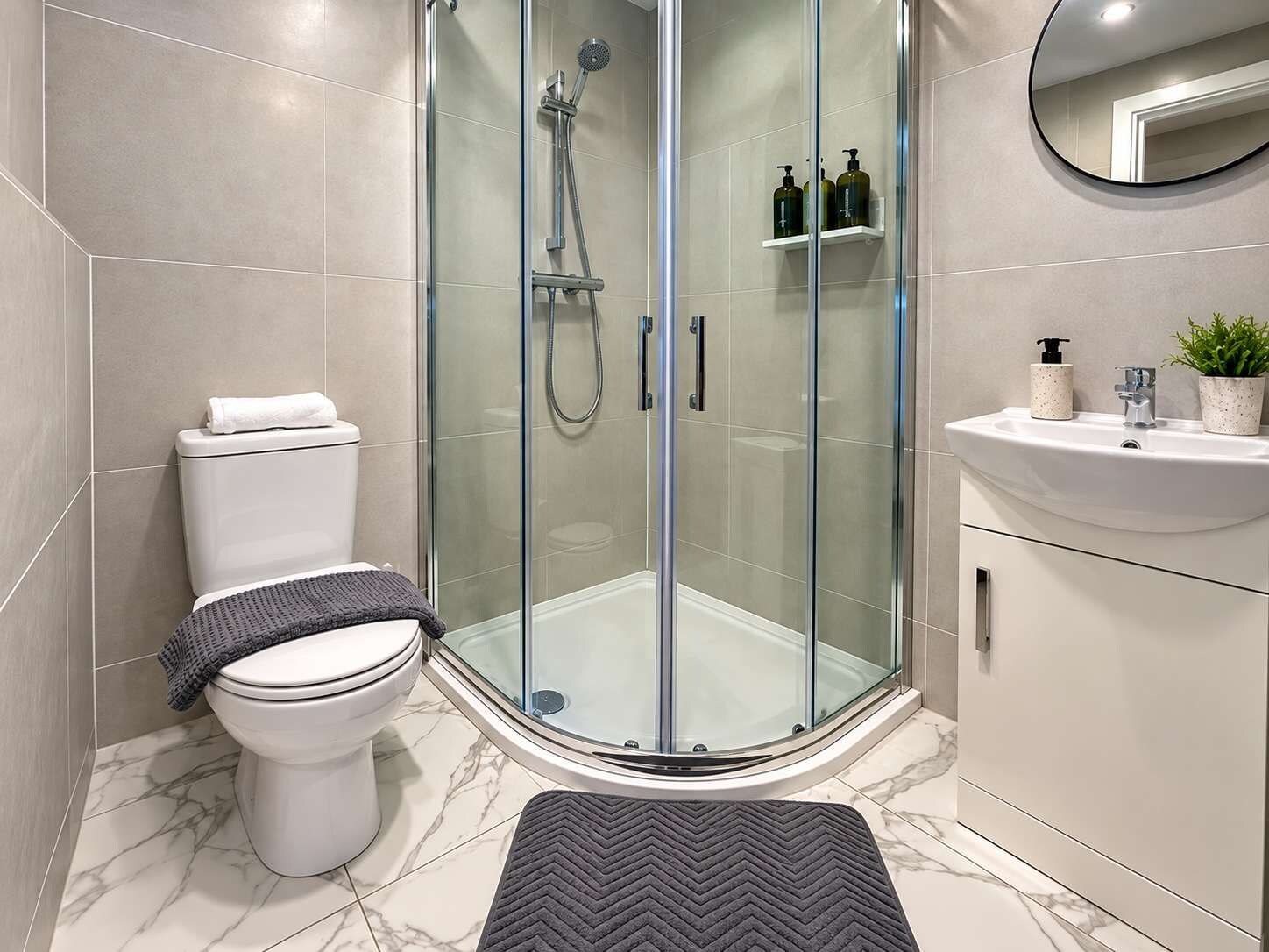 A modern bathroom with a glass-enclosed shower, a toilet, a sink with a mirror, and toiletries on a shelf.