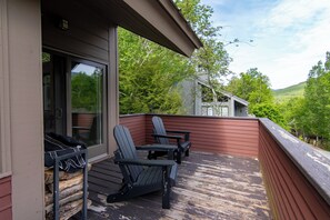 Eine Terrasse mit Adirondack-Stühlen und einem Tisch, mit Blick auf ein bewaldetes Gebiet.