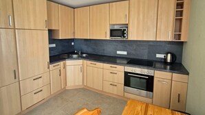 A compact kitchen with wooden cabinets, a microwave, a stove, and a dining table with a chair. - Vacation apartment Waldbronn 1 person (Waldbronn)
