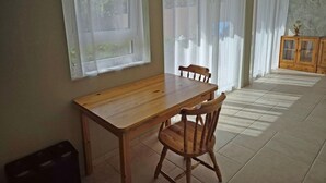 A dining area with a wooden table and chairs, large windows with white curtains, and a tiled floor. - Vacation apartment Waldbronn 1 person (Waldbronn)