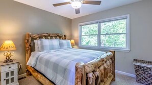A bedroom with a wooden bed frame, a ceiling fan, a window with a view of trees, and a bedside lamp. - Solace Mountain Cozy Mountain Retreat with Game Room, sleeps 9, Wifi, private (Franklin)