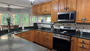 A kitchen with wooden cabinets, a stainless steel microwave, a stove, and a large window. - Solace Mountain Cozy Mountain Retreat with Game Room, sleeps 9, Wifi, private (Franklin)