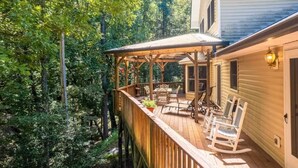 A wooden deck with outdoor furniture and a covered area, surrounded by dense trees. - Solace Mountain Cozy Mountain Retreat with Game Room, sleeps 9, Wifi, private (Franklin)