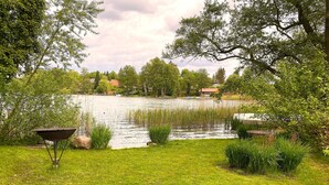 Ruohikkoalue, jossa on lampi, ja jonka ympärillä on puita sekä muutamia rakennuksia kauempana taustalla.