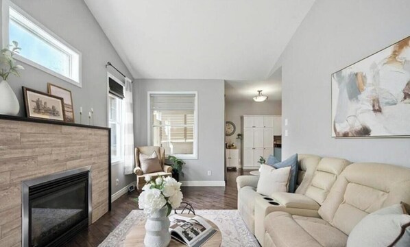 A living room with a fireplace, a sofa, a coffee table with a vase and book, and a painting on the wall.