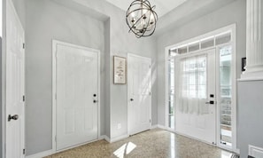A hallway with white doors, a chandelier, and a framed picture on the wall.