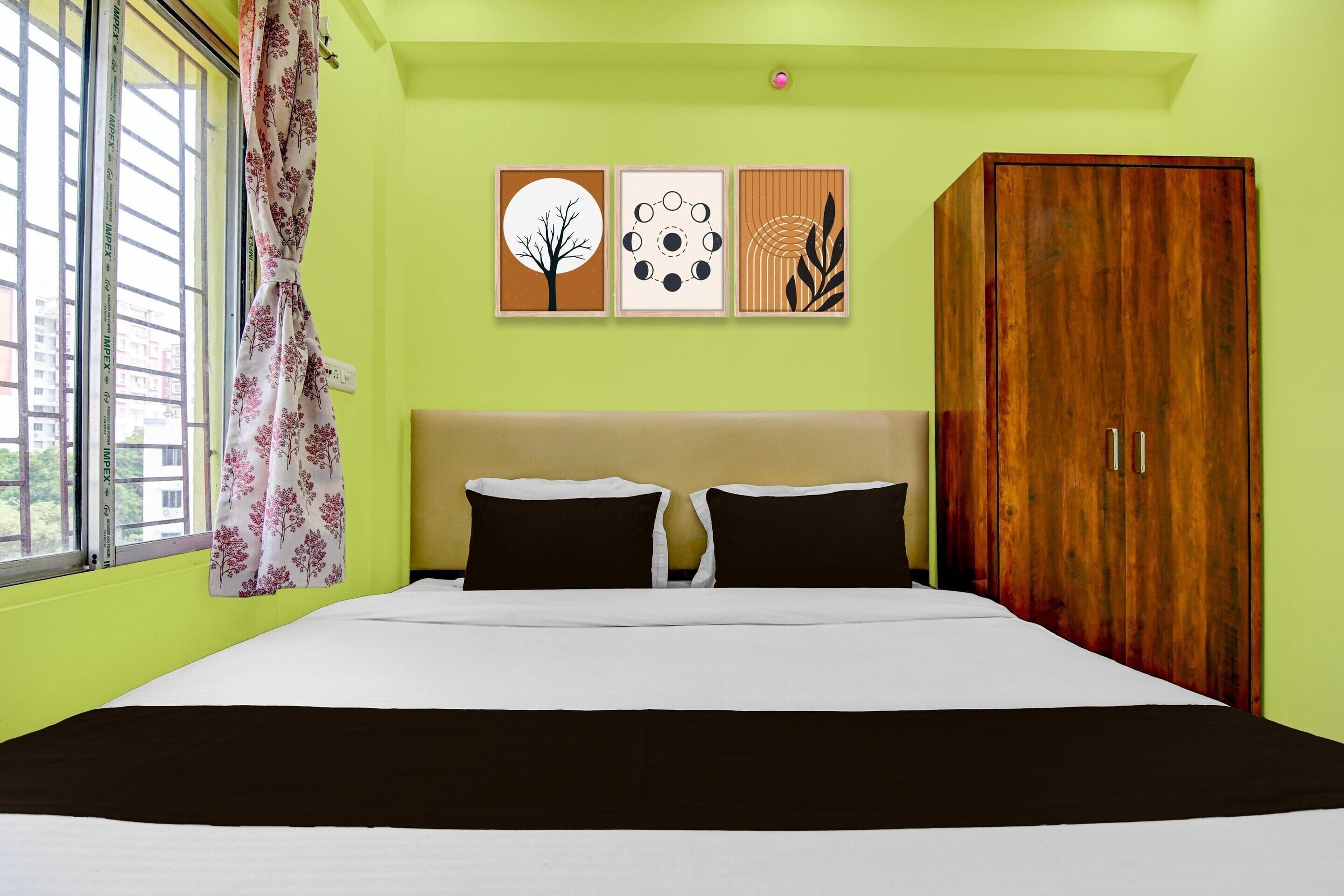 A bedroom with a bed, a wardrobe, a window with curtains, and three framed pictures on the wall.