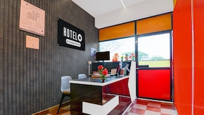 Een receptiebalie van een hotel met een 'HOTELO' bord, een kalender, een flatscreen-tv en een raam met uitzicht op groen.