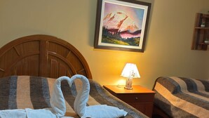 Een hotelkamer met twee bedden, een schilderij aan de muur, een lamp op het nachtkastje, en handdoeken netjes opgemaakt op de bedden.