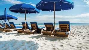 Sedie da spiaggia numerate 1001 e 1002 con ombrelloni blu su una spiaggia sabbiosa.