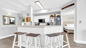 Una cucina moderna con mobili bianchi, un'isola centrale con sgabelli da bar, un forno a microonde e un frigorifero.