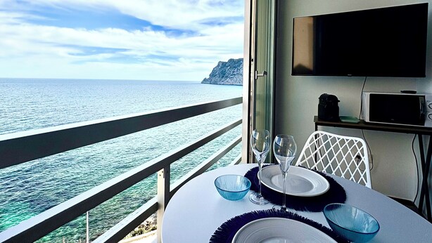 A balcony with a view of the sea, a table set with plates and glasses, a TV mounted on the wall, and a microwave on a small table. - Mediterranean Dream Calpe (Calp)