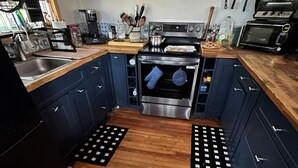 A kitchen with wooden flooring, blue cabinets, a stove, oven, and various kitchen utensils.