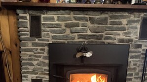 A stone fireplace with a fire, a wooden mantel, and a metal grate above it.