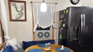 A dining area with a round wooden table, blue placemats, a black refrigerator, and a wall clock.