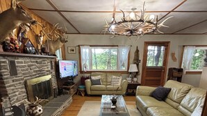 A cozy living room with a stone fireplace, a leather sofa, a coffee table, and a chandelier.