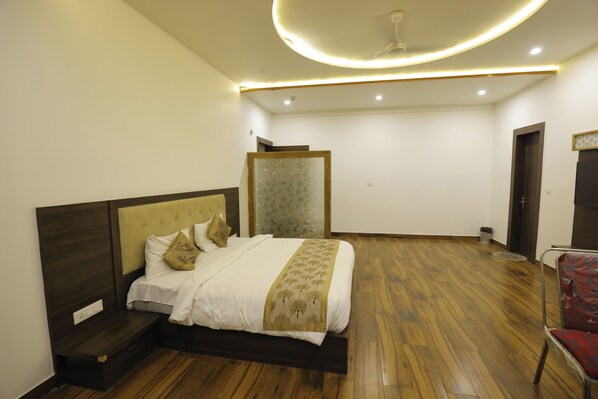 Quarto com cama, piso de madeira, luminária no teto, porta e uma cadeira.