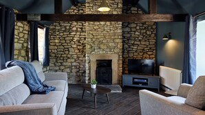Una sala de estar con pared de piedra, chimenea, sofá, mesa de centro y televisor.
