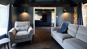 Una sala de estar moderna con un sofá, un sillón y una mesita. Se ve una cocina al fondo.
