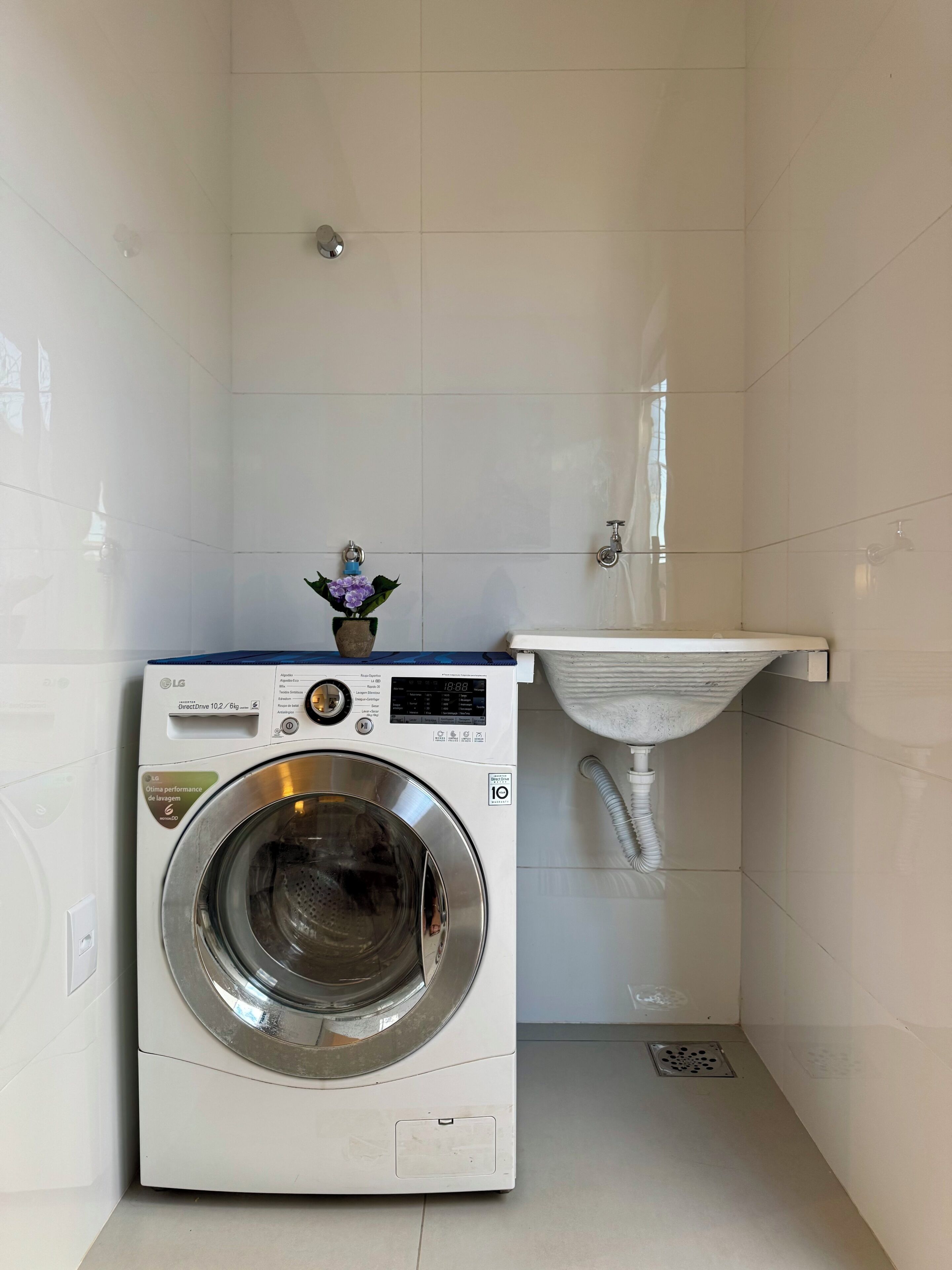 Um espaço compacto para lavanderia, com máquina de lavar, pia e uma pequena planta decorativa.