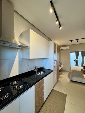 Une cuisine moderne équipée d’une cuisinière à gaz, d’un évier et de meubles blancs. On y trouve également un coin repas avec une table et des chaises, ainsi qu’une chambre à coucher avec un lit et des rideaux.