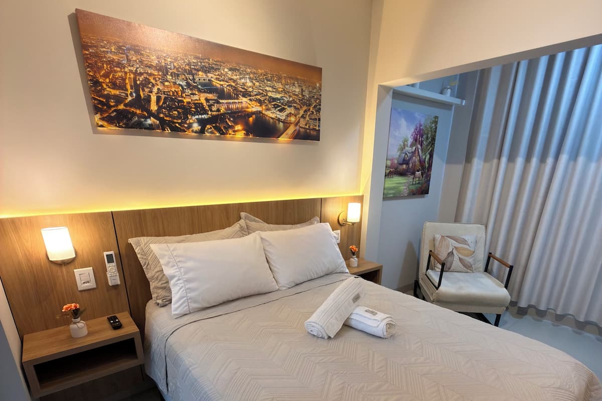 Ein Hotelzimmer mit einem großen Bett, einem Nachttisch mit Lampe, einem Sessel und einem Gemälde an der Wand.