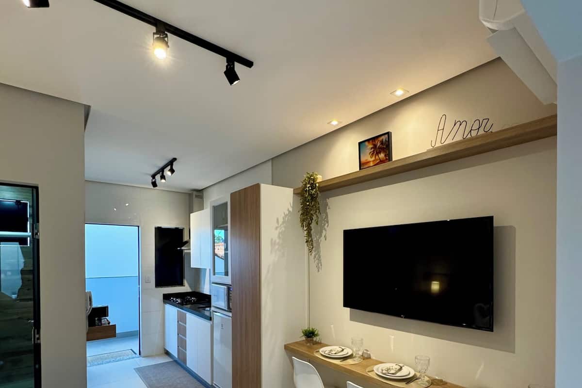 Ein modernes Hotelzimmer mit einem Bett, einem Essbereich mit Stühlen und einem Tisch, einem an der Wand befestigten Fernseher und einer Küchenzeile.