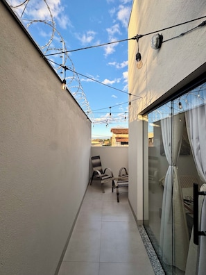 Un balcón estrecho con una silla, un vidrio y luces colgantes.