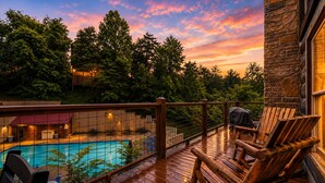 Eine Holzterrasse mit Pool, Stühlen und einem Steinhaus.
