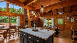 Ein Holzblockbau-Innenraum mit einem großen Esstisch, Holzsesseln, einer Kochinsel mit Spüle und einem Deckenventilator.
