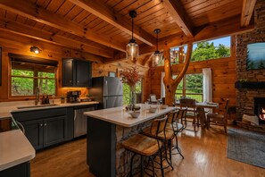 Interior de una cabaña de madera con cocina, comedor y chimenea.