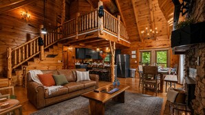 Ein Holzblockhaus-Interieur mit einer Holzwindeltreppe, einem Essbereich, einer Küche und einem Kamin.