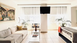 Un salon moderne avec un canapé, une table basse, un téléviseur et de grandes fenêtres.