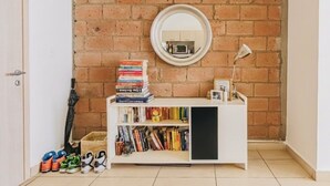 Une pièce avec un mur en briques, une bibliothèque blanche, un miroir et une porte.