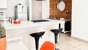 Une cuisine moderne dotée d’un îlot central, de tabourets de bar, d’un luminaire suspendu et d’un mur d’accent en briques.