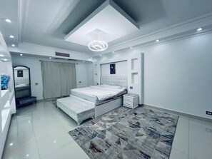 A modern bedroom with a large bed, a bedside table, a mirror, and a ceiling light fixture. - ELITE Premium 6BR Family Villa with Pool (New Cairo)