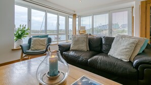 Un salon moderne avec un canapé en cuir, un porte-bougie en verre et une vue sur la mer grâce à de grandes fenêtres.