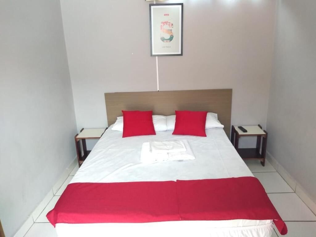 Una cama bien hecha con ropa de cama roja y blanca, dos mesitas de noche y un cuadro enmarcado en la pared.