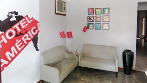 A hotel lobby with a sofa, a wall-mounted map, a vent, and a row of framed pictures. - América Hotel Jacareí (Jacareí)