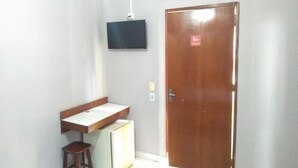 A room with a wooden door, a small stool, a white table, and a mounted television. - América Hotel Jacareí (Jacareí)