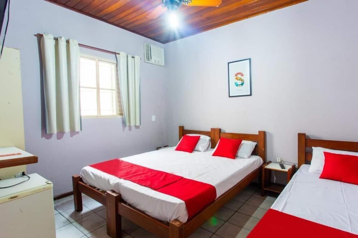 Una habitación con dos camas, una ventana con cortinas, un escritorio pequeño y un refrigerador.