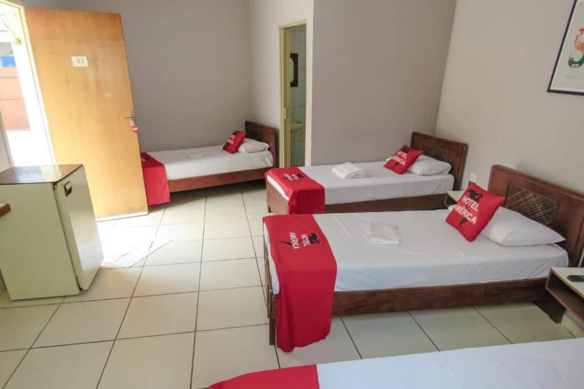 Habitación de hotel con tres camas individuales, un escritorio pequeño y un armario.