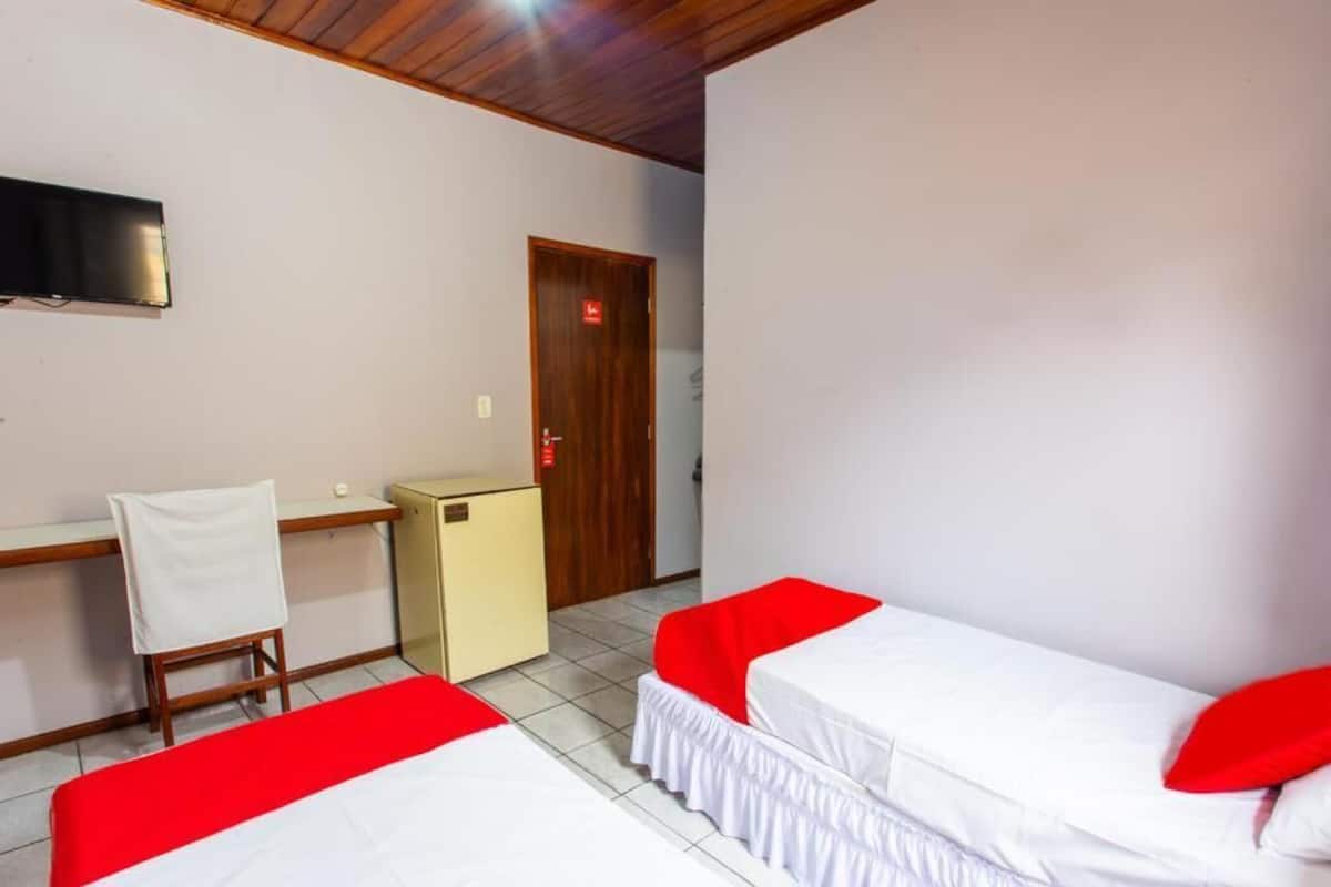 Habitación de hotel con dos camas, un escritorio, una silla, un televisor y una puerta con luz roja.