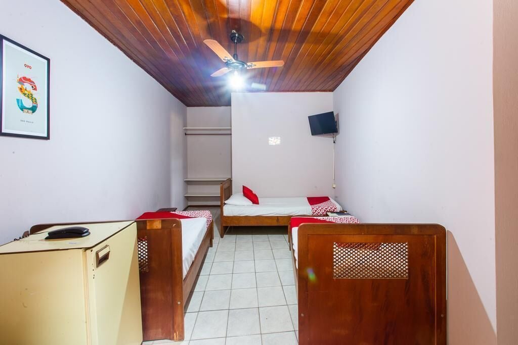 Een kleine kamer met twee bedden, een plafondventilator, een televisie aan de muur en een bureau met een computer.