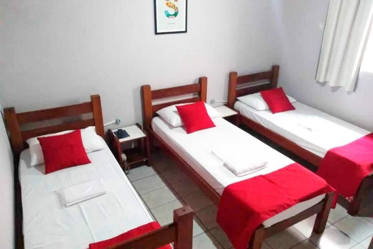 Una habitación con tres camas de madera, cada una con almohada roja y ropa de cama blanca.