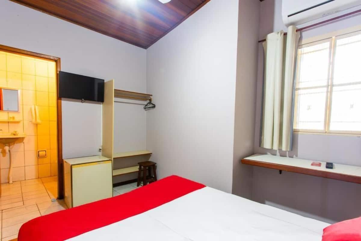 Un dormitorio con cama, escritorio, silla, televisor y ventana.