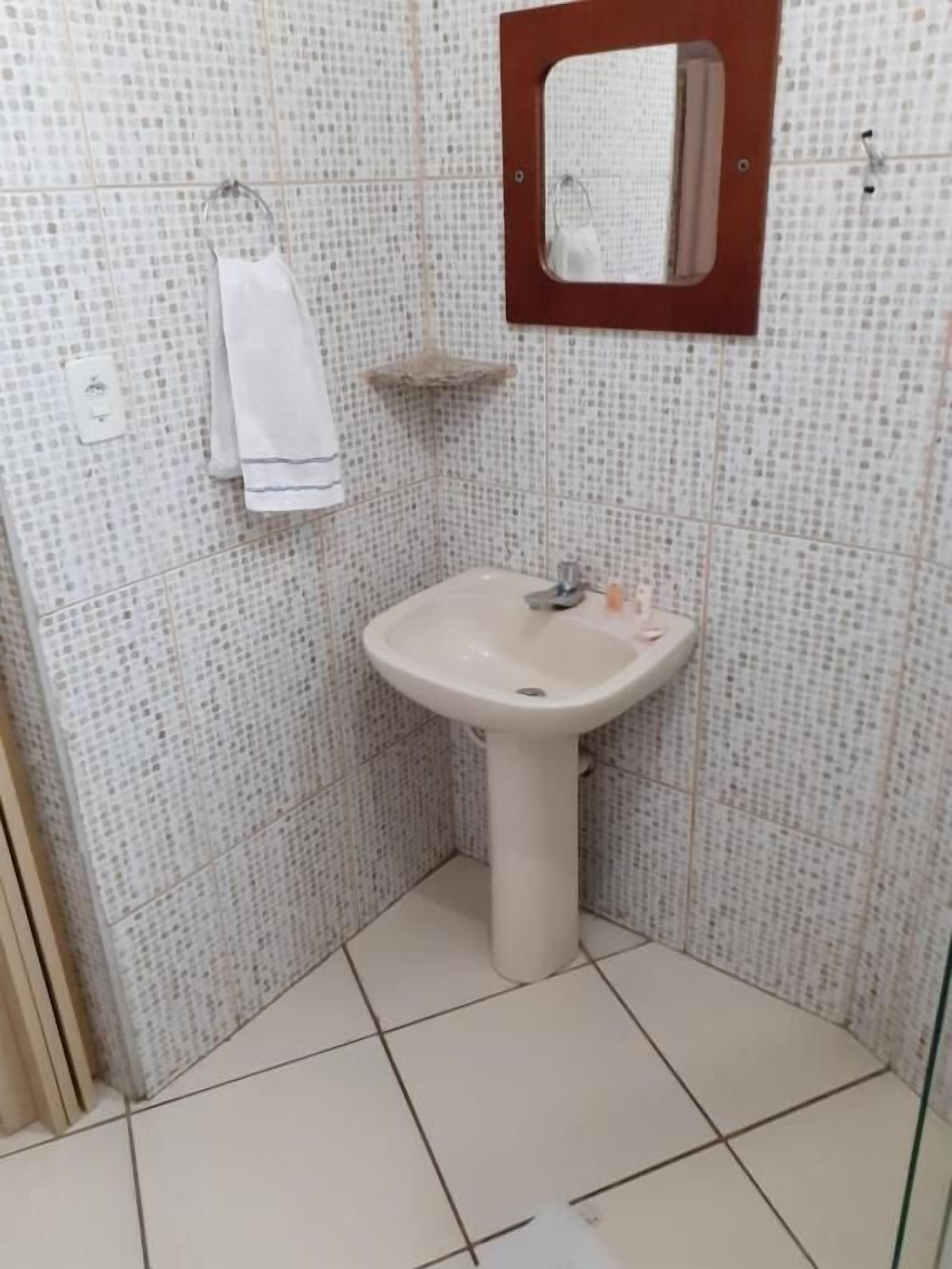Uma casa de banho com lavatório branco, espelho e barra de toalhas.