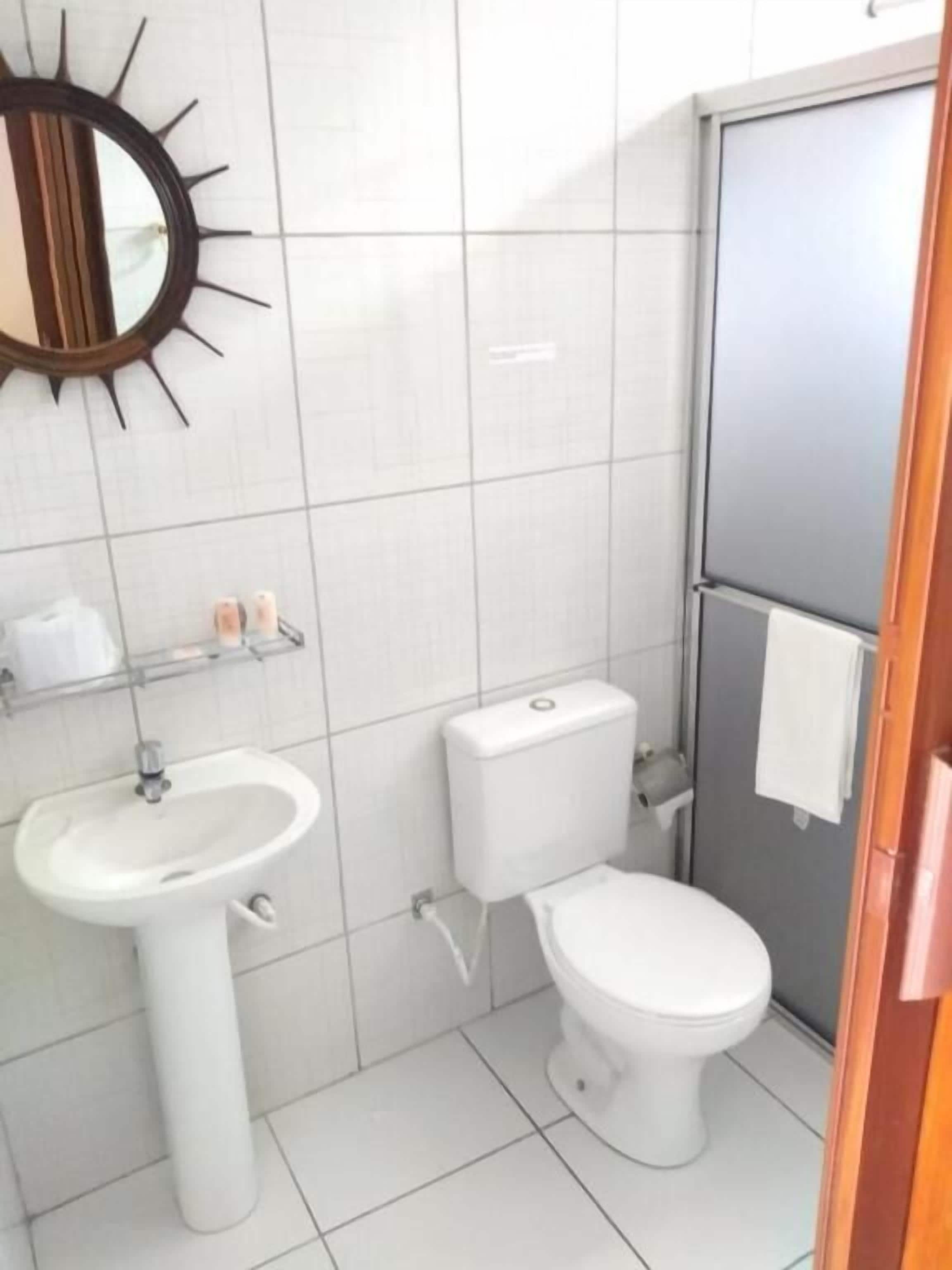 A bathroom with a white sink, toilet, and a mirror with a sunburst design.