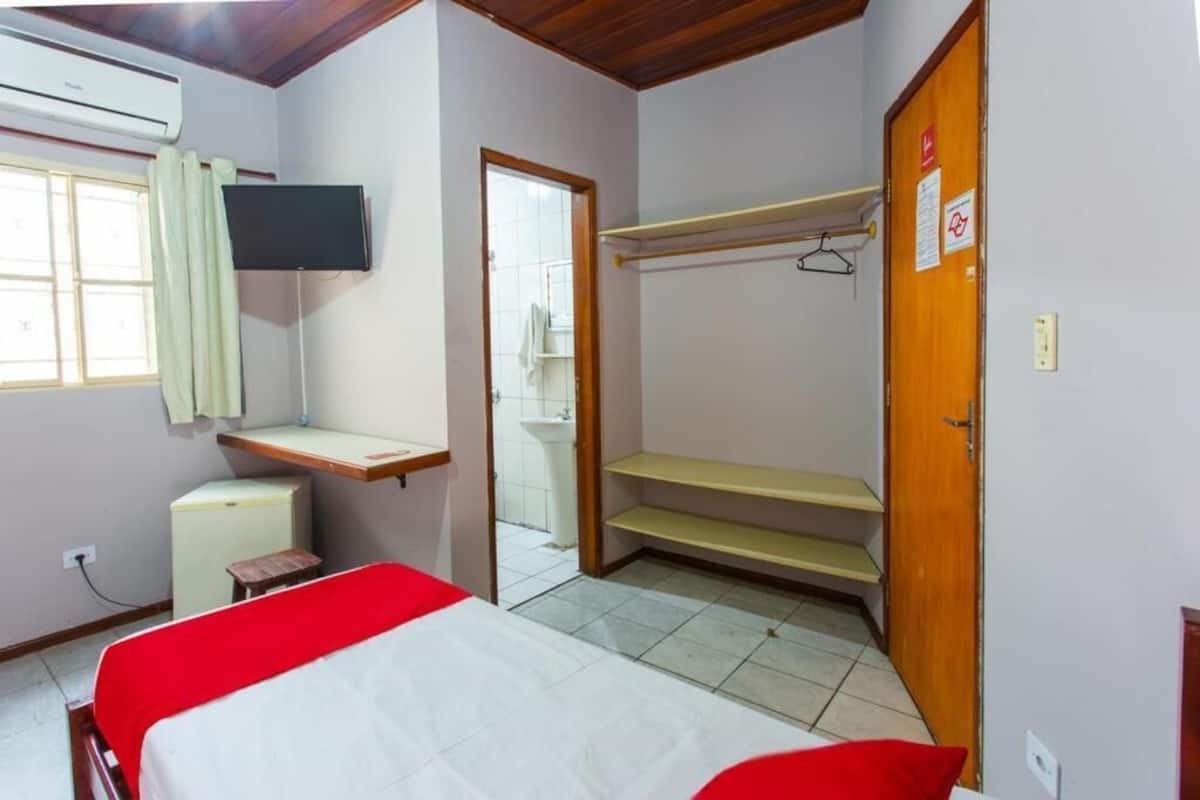 Una habitación con cama, televisor, escritorio, armario y espejo.